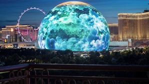 Een grote, verlichte bol met een bewolkte textuur, een reuzenrad en het Venetian hotel op de achtergrond.