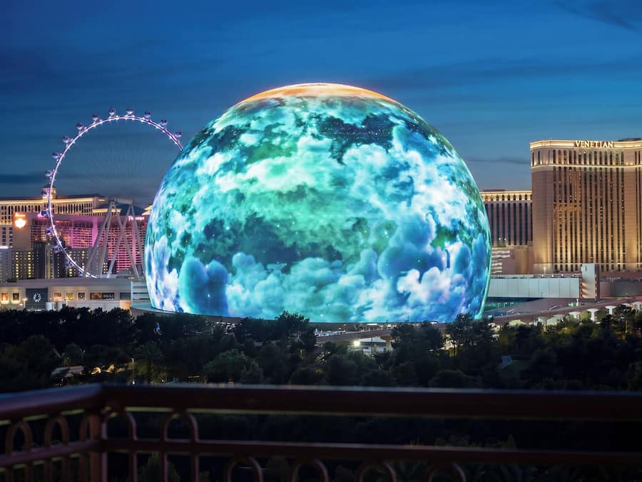Uma esfera grande e iluminada com textura de nuvens, uma roda-gigante e o hotel Venetian ao fundo.