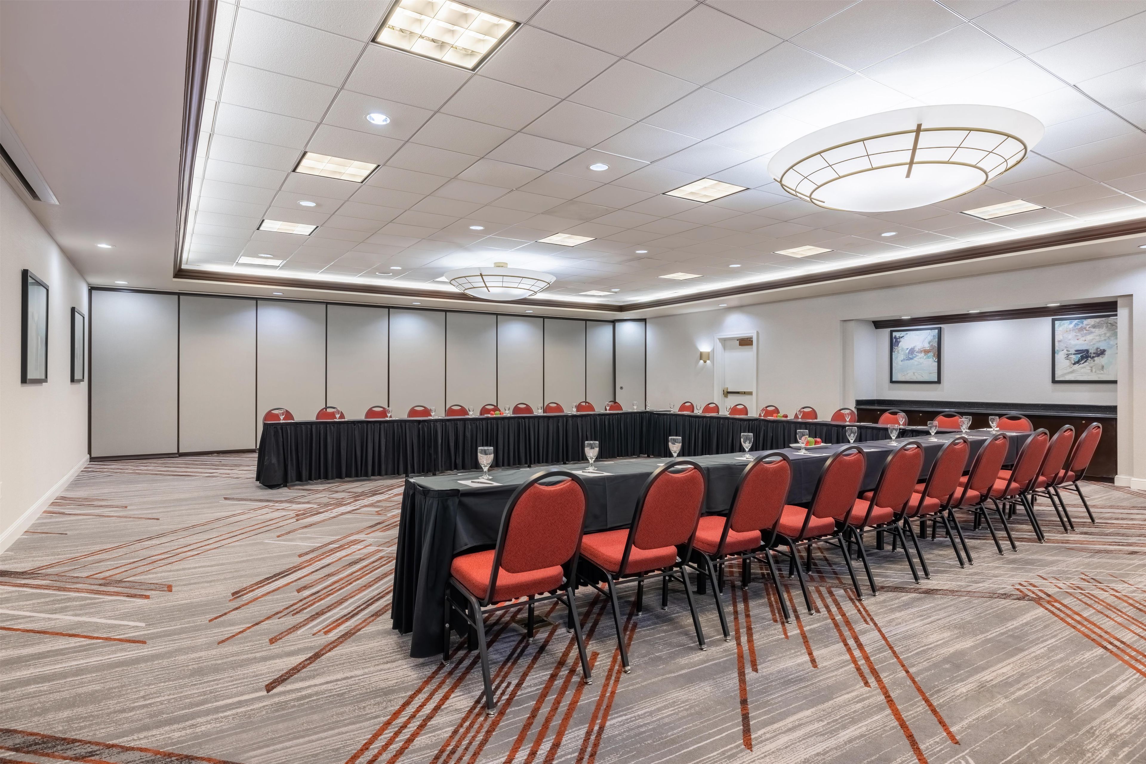 A conference room with a long table, red chairs, and a projector screen.
