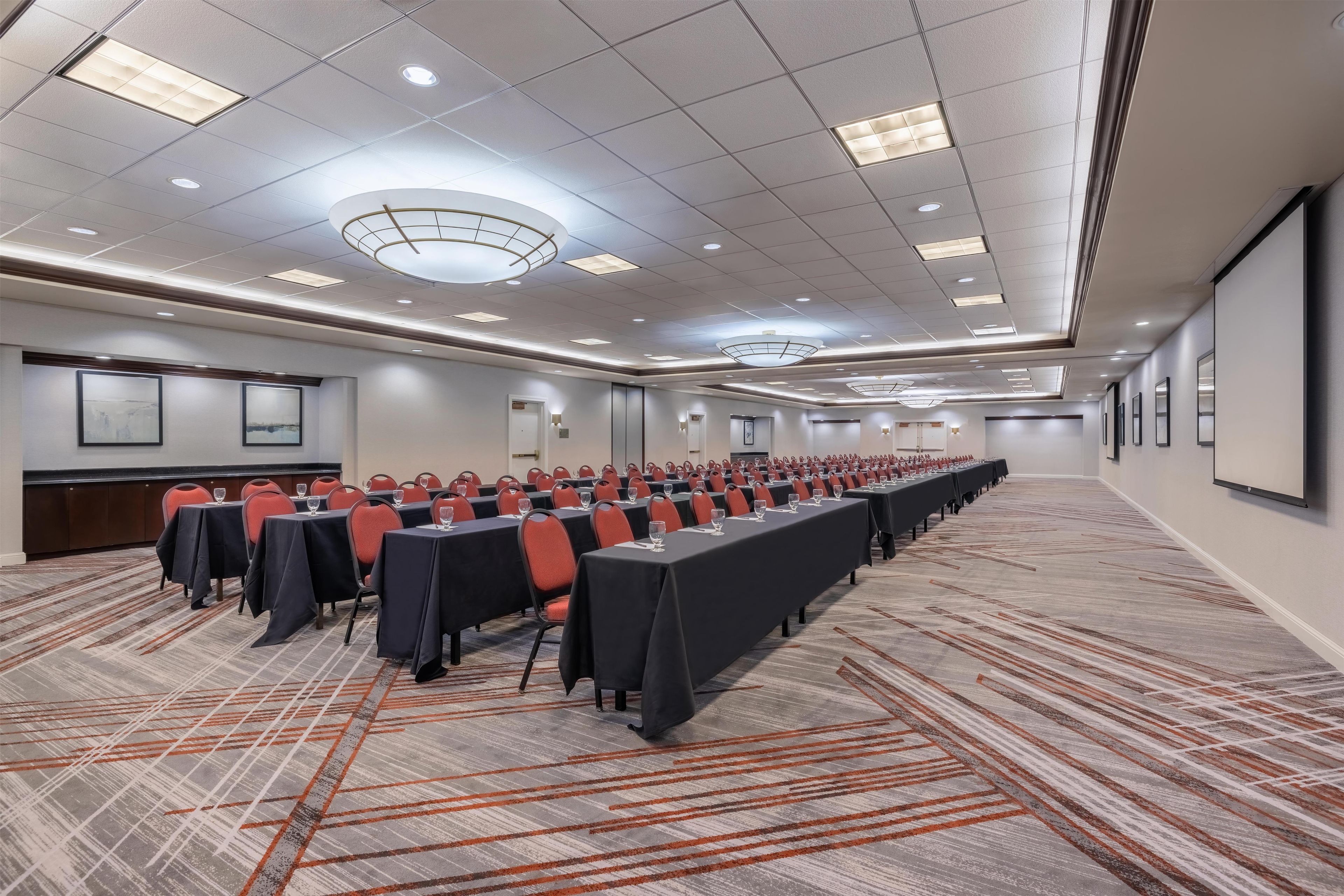 A conference room with long tables, chairs, and a carpeted floor.