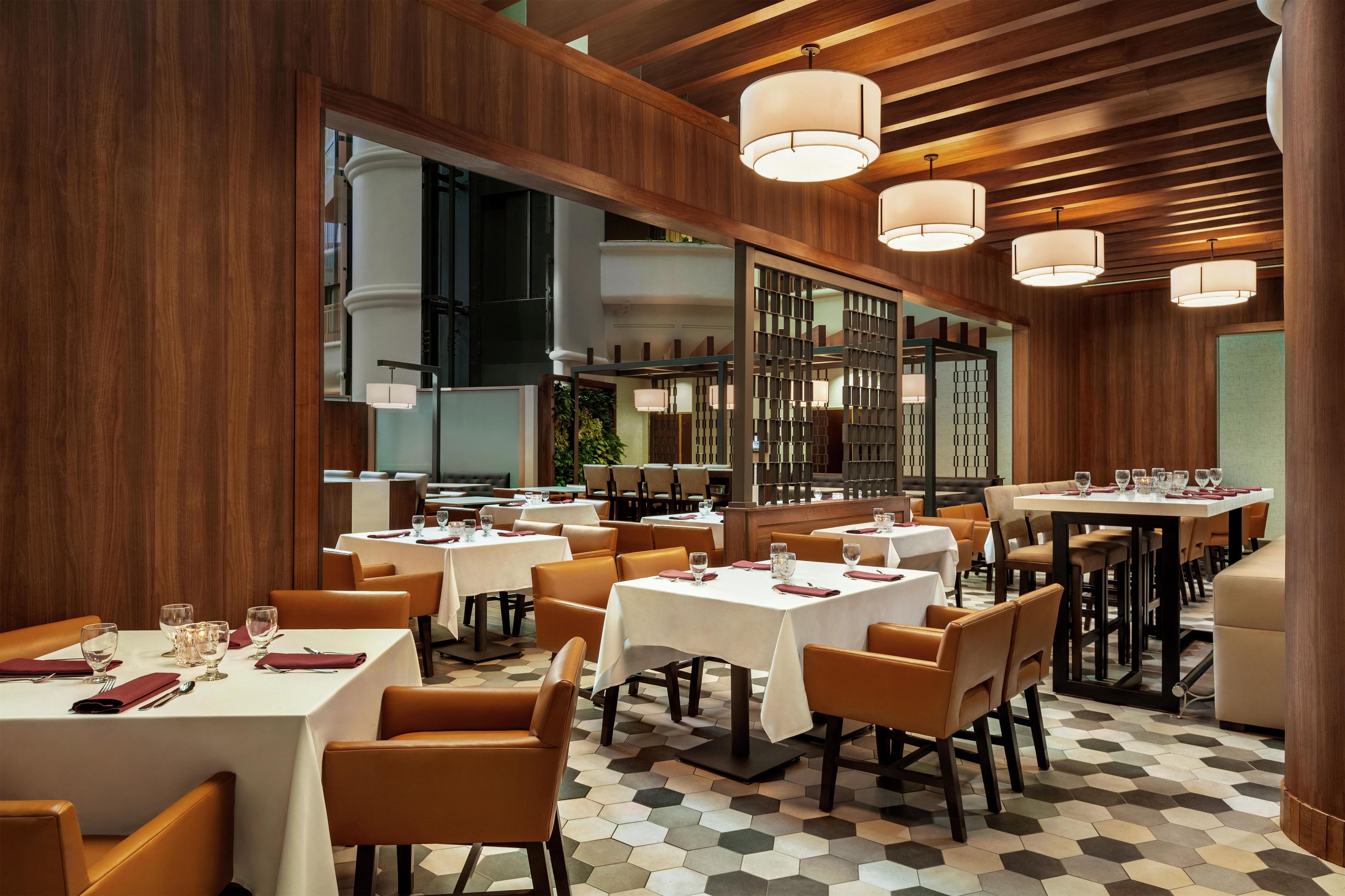 A restaurant interior with multiple tables, chairs, and pendant lighting.