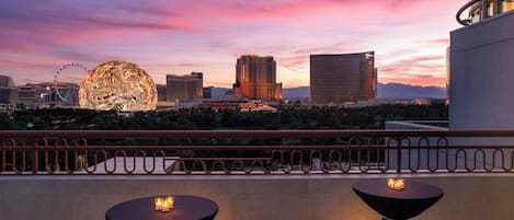 A rooftop terrace with two round tables, a Ferris wheel, and a city skyline at dusk.