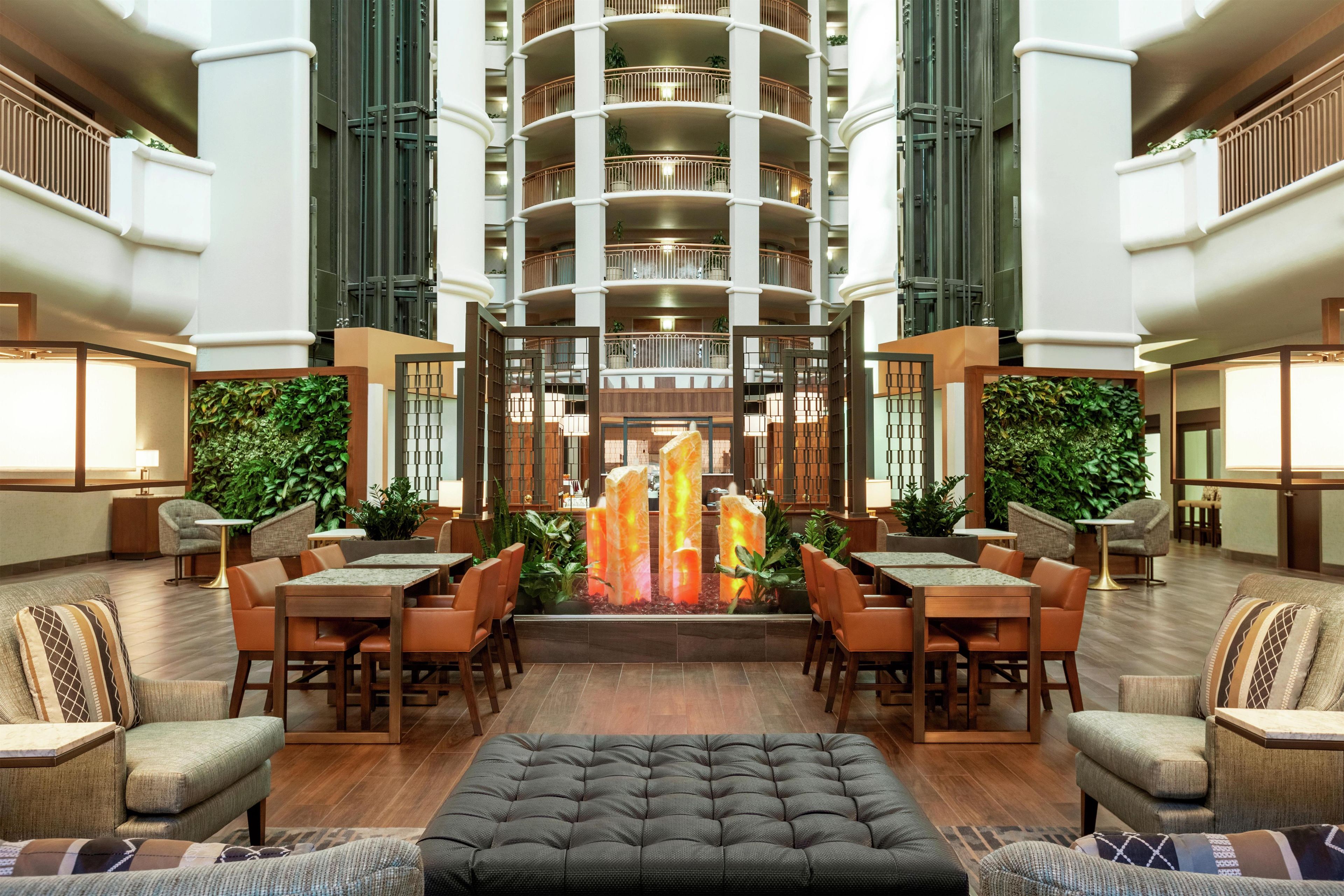 A hotel lobby with a central seating area, multiple floors of balconies, and lush greenery.