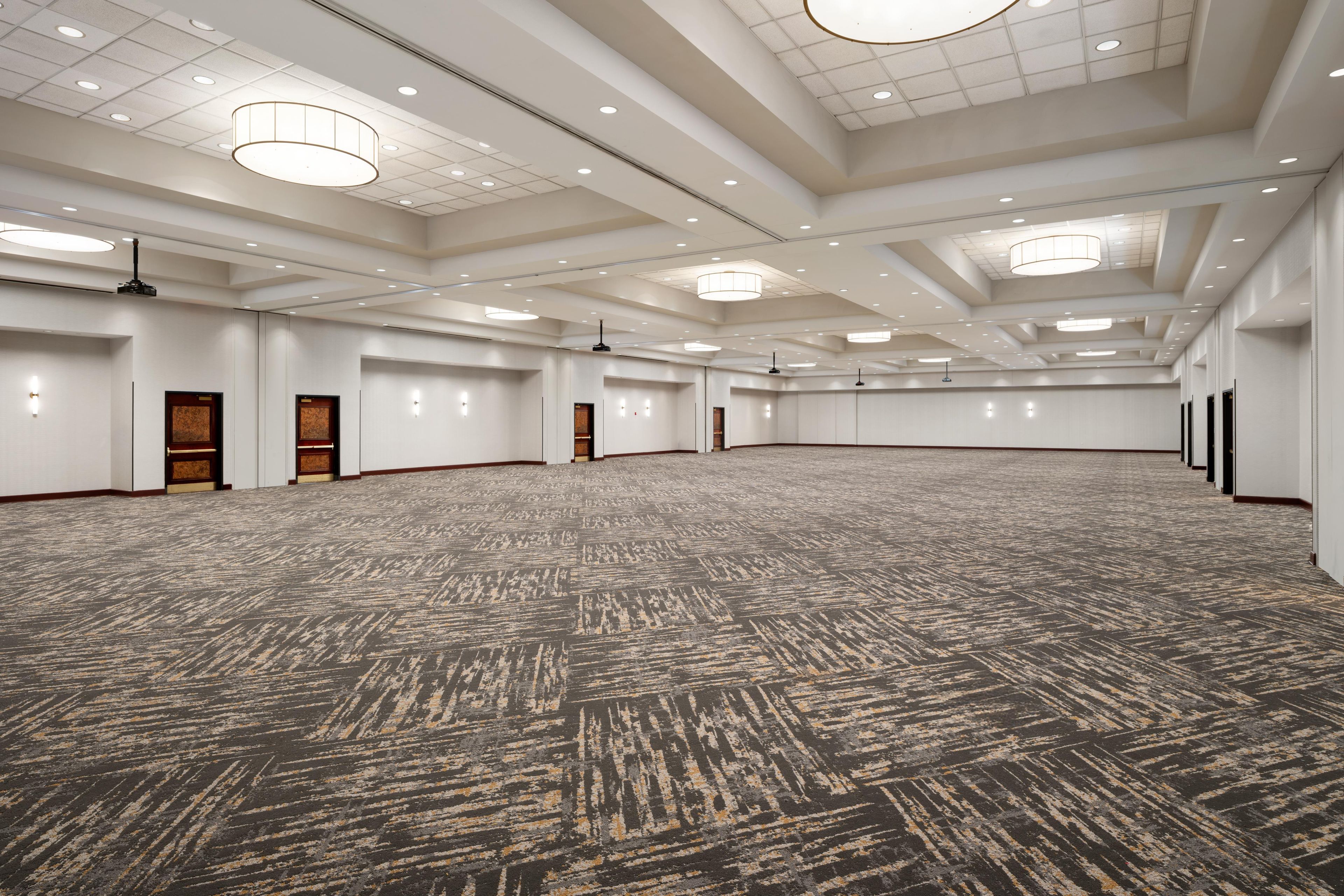 A large, empty conference room with a patterned carpet, recessed lighting, and a high ceiling.