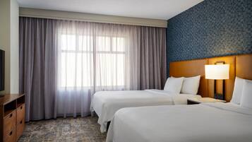 A hotel room with two beds, a television, a desk, and a patterned carpet.