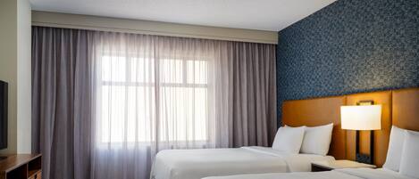 Una habitación de hotel con dos camas, televisión, escritorio y alfombra estampada.