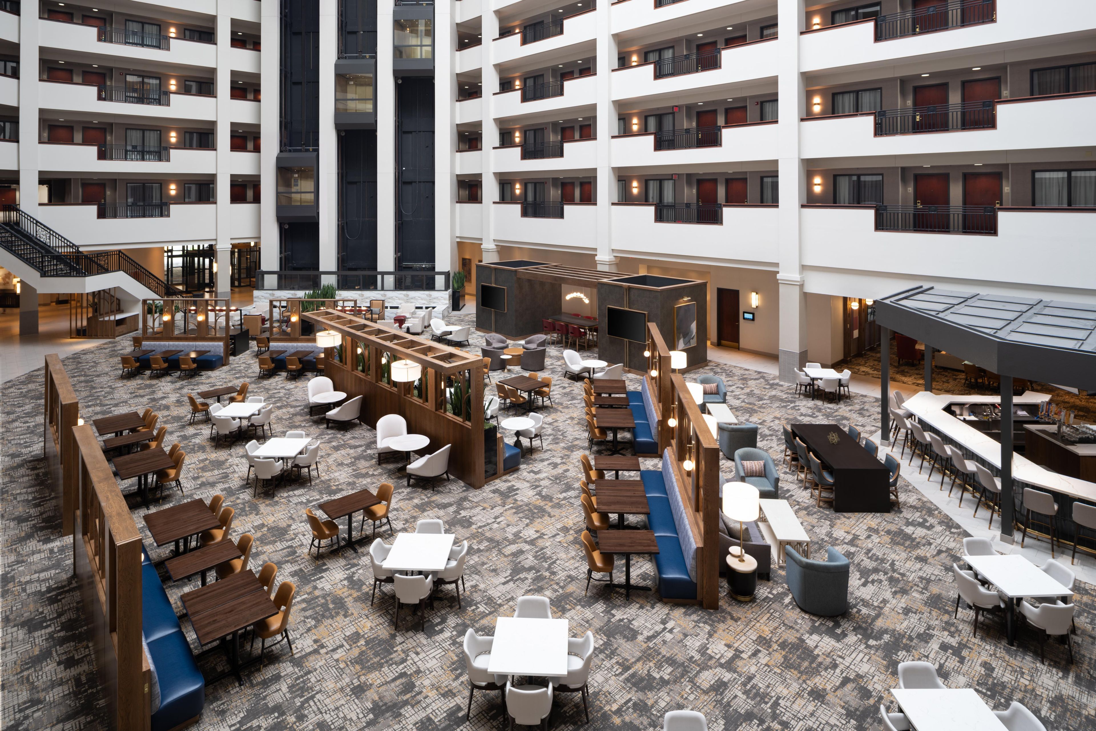Un hall de hotel espacioso con varias zonas de restauración, un área central de estar y una escalera que conduce a plantas superiores.
