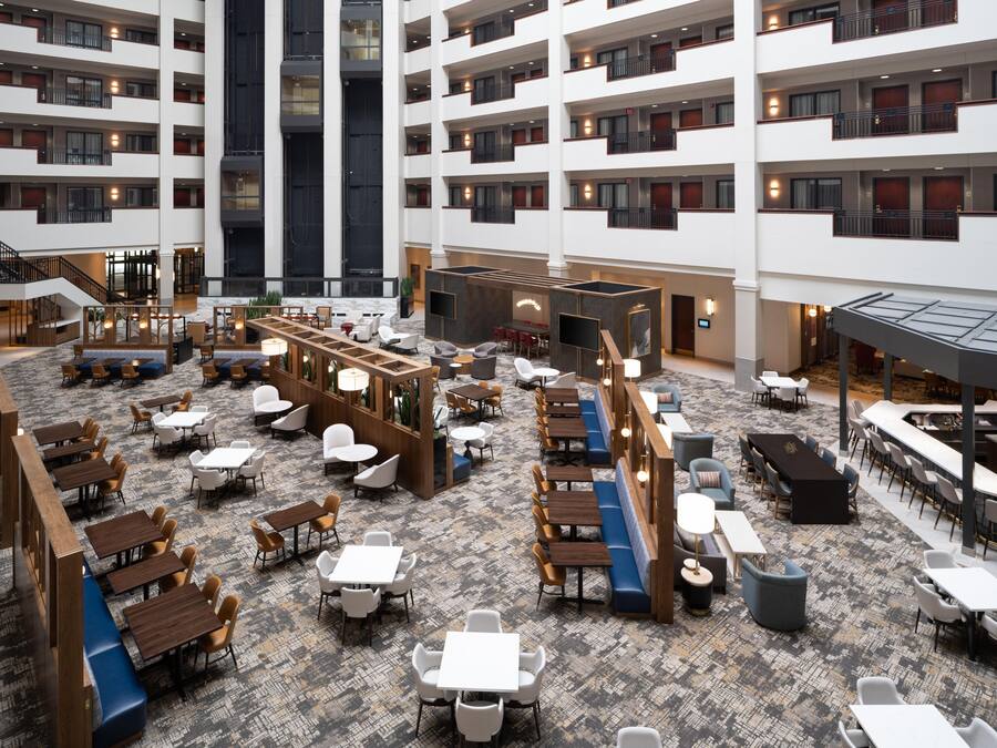 A spacious hotel lobby with multiple dining areas, a central seating area, and a staircase leading to upper floors.