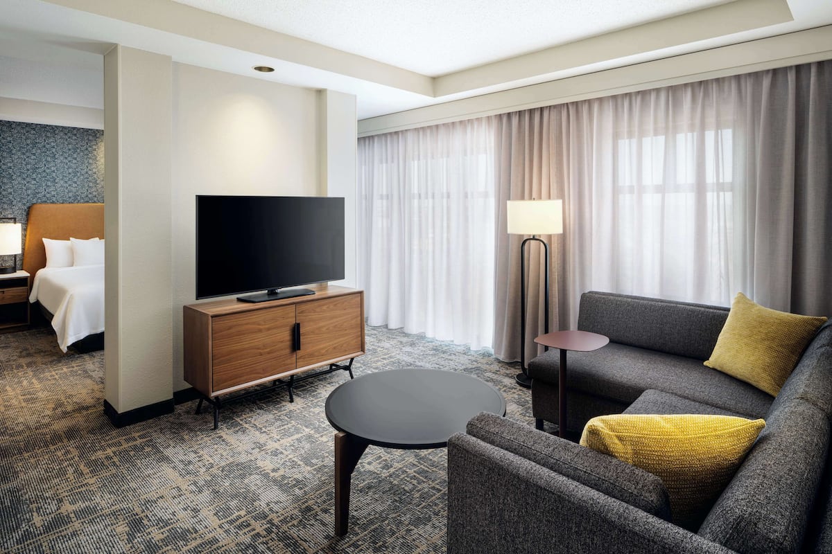 A hotel room with a bed, a TV, a sofa, a coffee table, and a lamp.