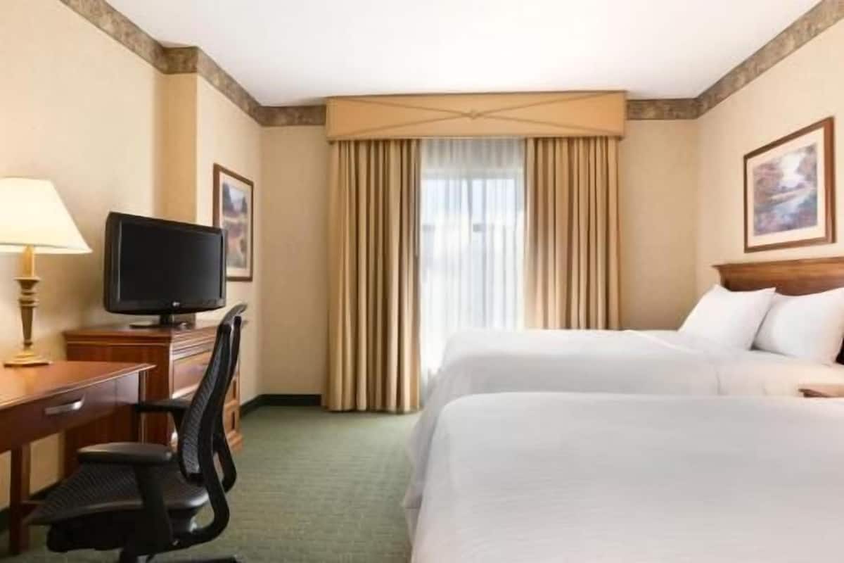 A hotel room with two beds, a desk with a television, and a window with curtains.