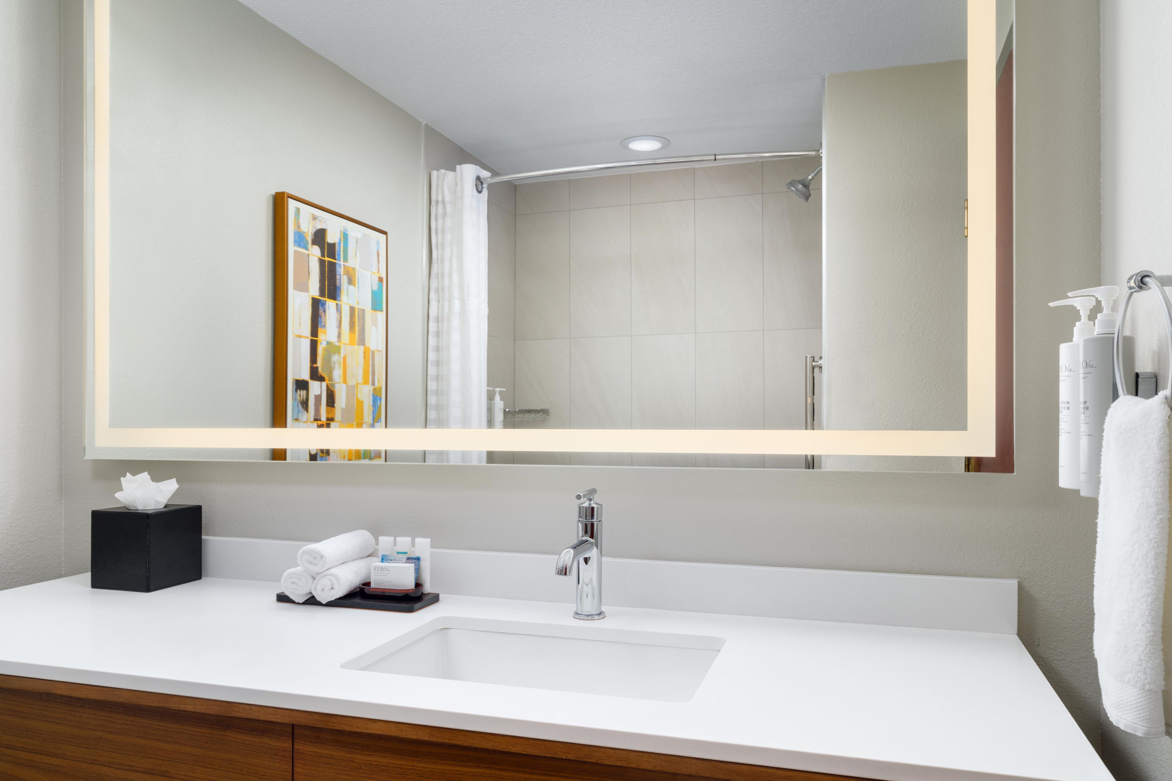 A modern bathroom with a large mirror, a white sink, and a shower.