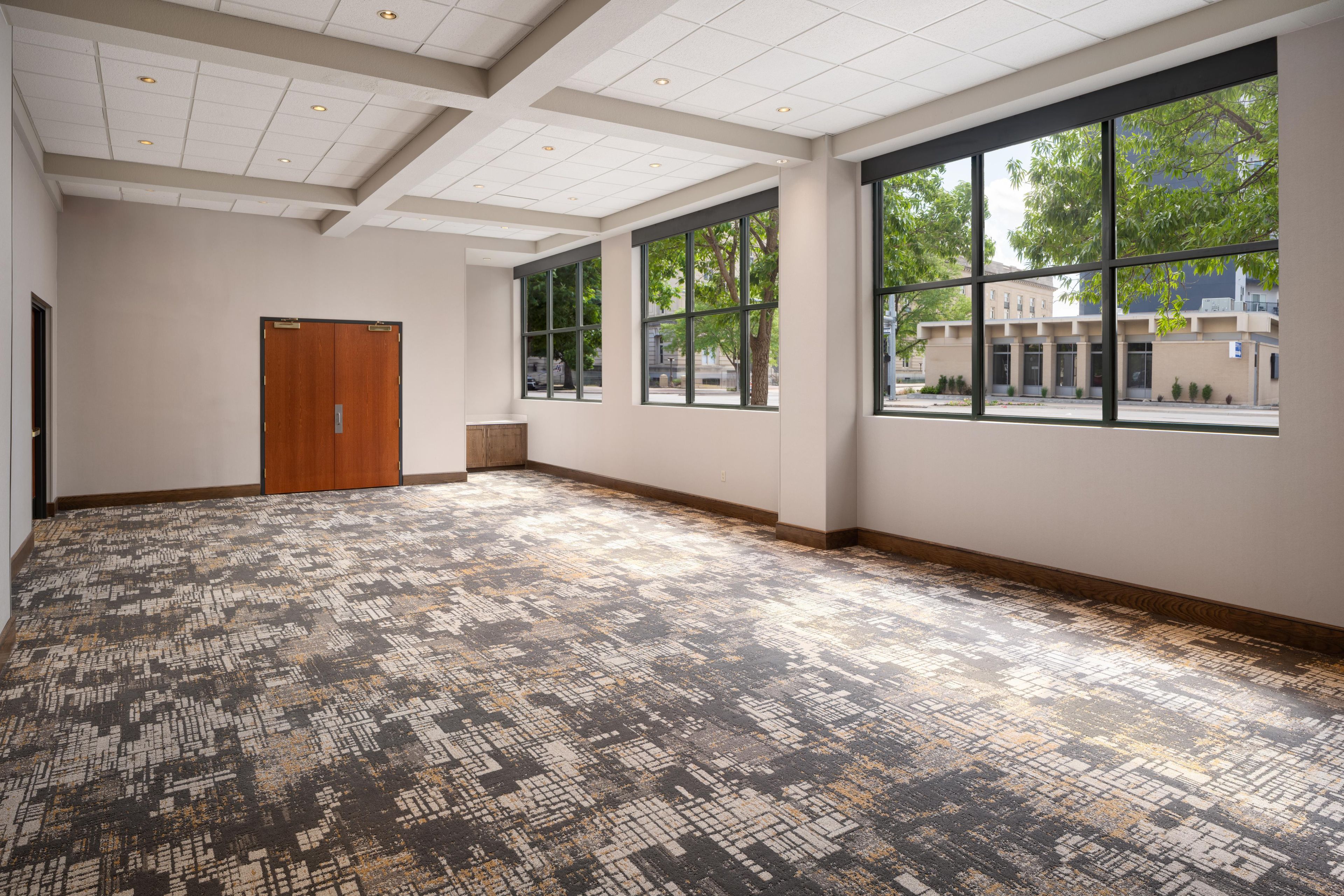 A spacious room with large windows, a door, and patterned carpet.