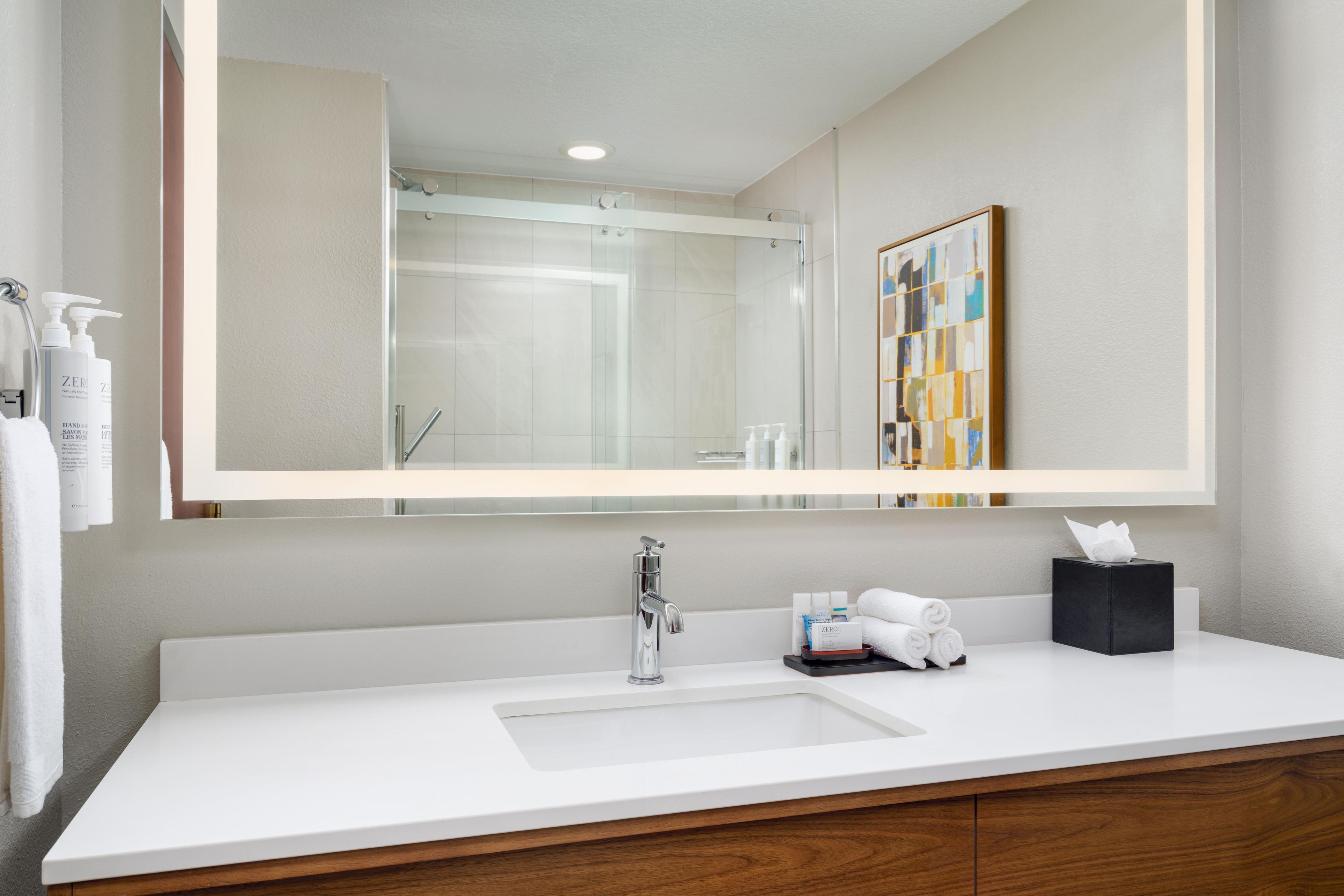 A modern bathroom with a large mirror, a white sink, and a wooden vanity.