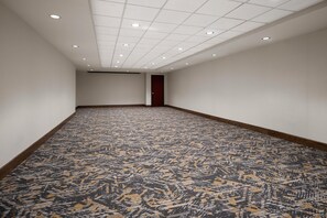 Un pasillo con alfombra estampada, paredes blancas y una puerta de madera al final.