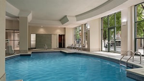Una piscina interna con acqua cristallina, circondata da un solarium piastrellato e un’area salotto con sedie.