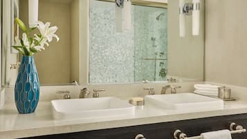 A bathroom with two sinks, a large mirror, a vase with flowers, and a shower area.