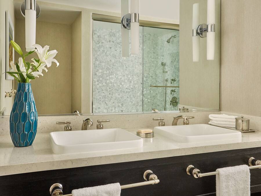 A bathroom with two sinks, a large mirror, a vase with flowers, and a shower area.