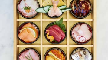 Una bandeja de madera con nueve recipientes que contienen diferentes tipos de sashimi y sushi.