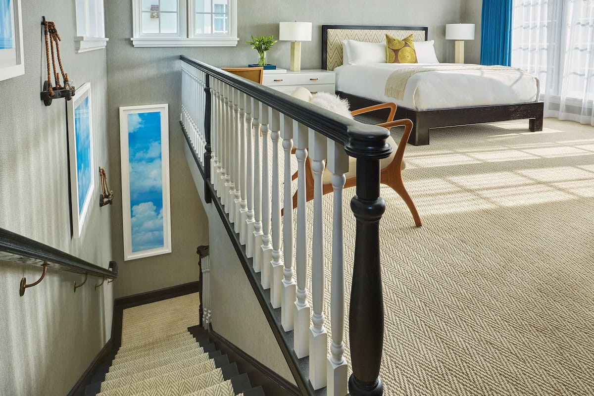 A bedroom with a large bed, a nightstand, a dresser, and a staircase with a railing.