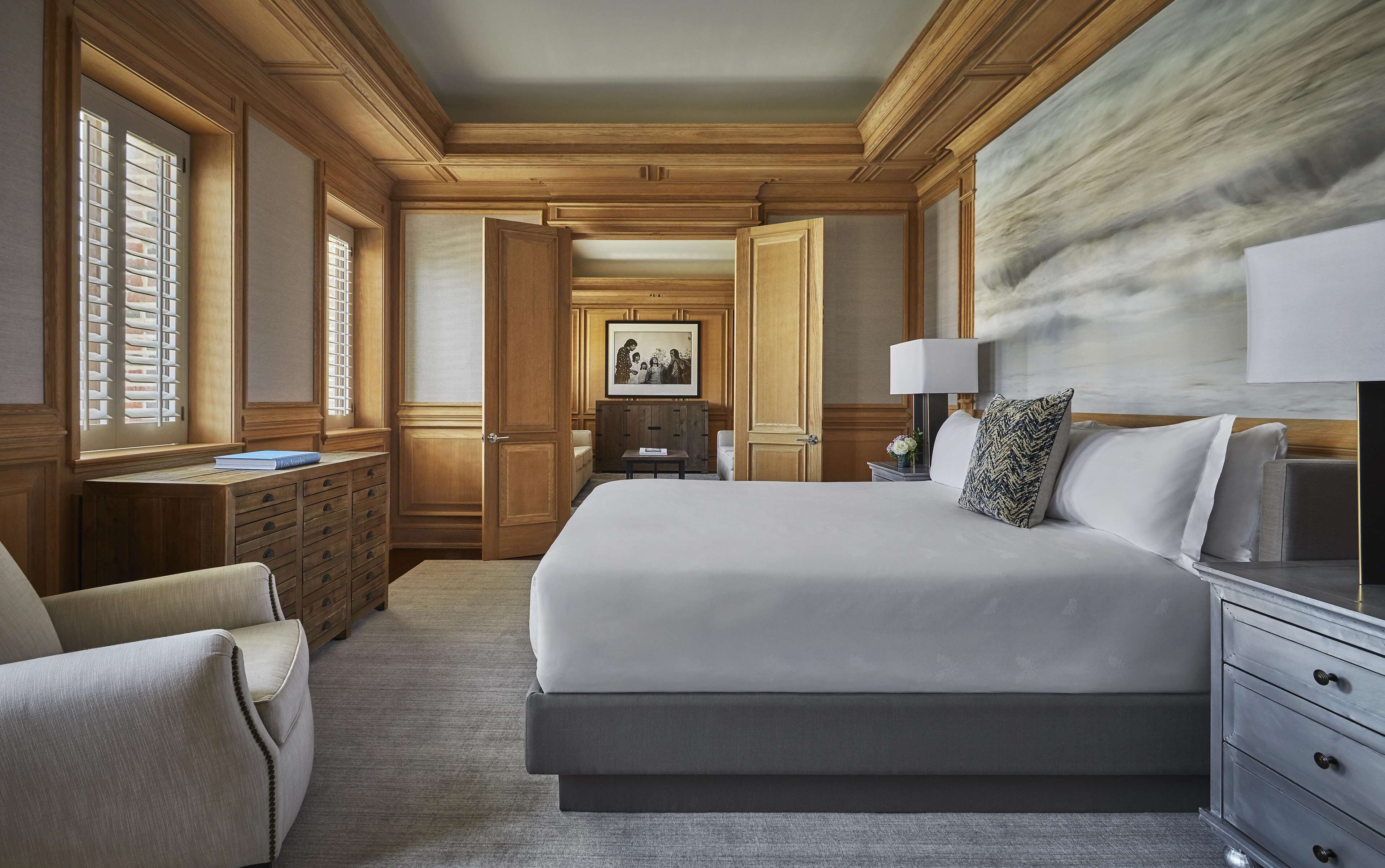 Une chambre d’hôtel spacieuse, dotée d’un grand lit, d’un bureau avec une lampe et donnant sur le couloir.
