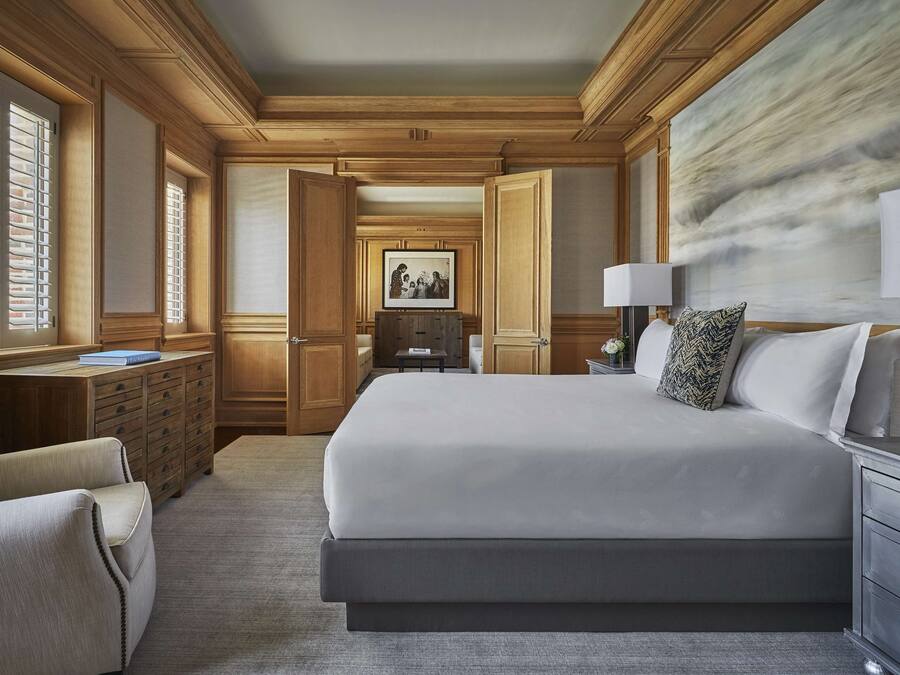 Une chambre d’hôtel spacieuse, dotée d’un grand lit, d’un bureau avec une lampe et donnant sur le couloir.