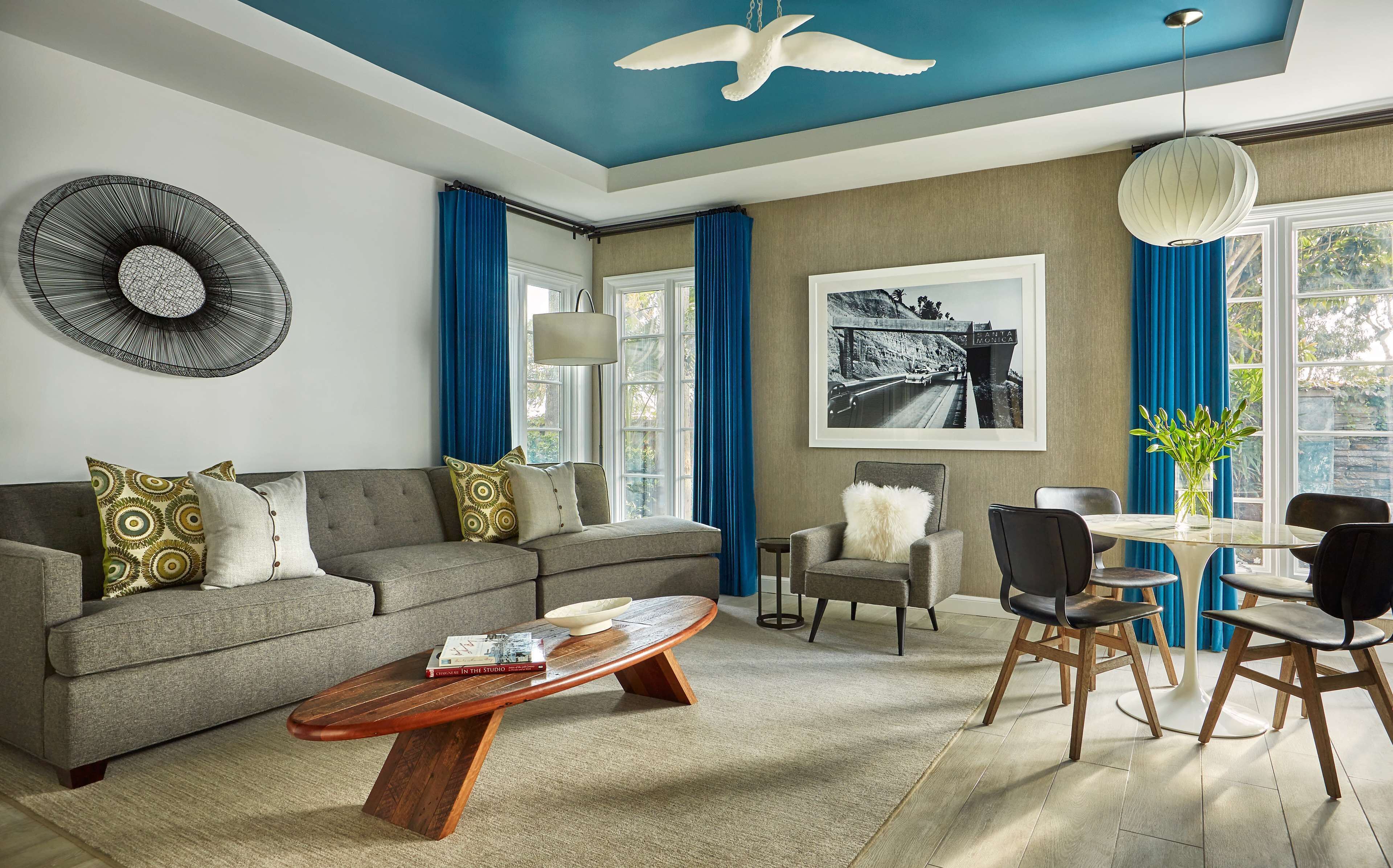 A modern living room with a grey sofa, a wooden coffee table, and a dining area with a glass table and chairs.