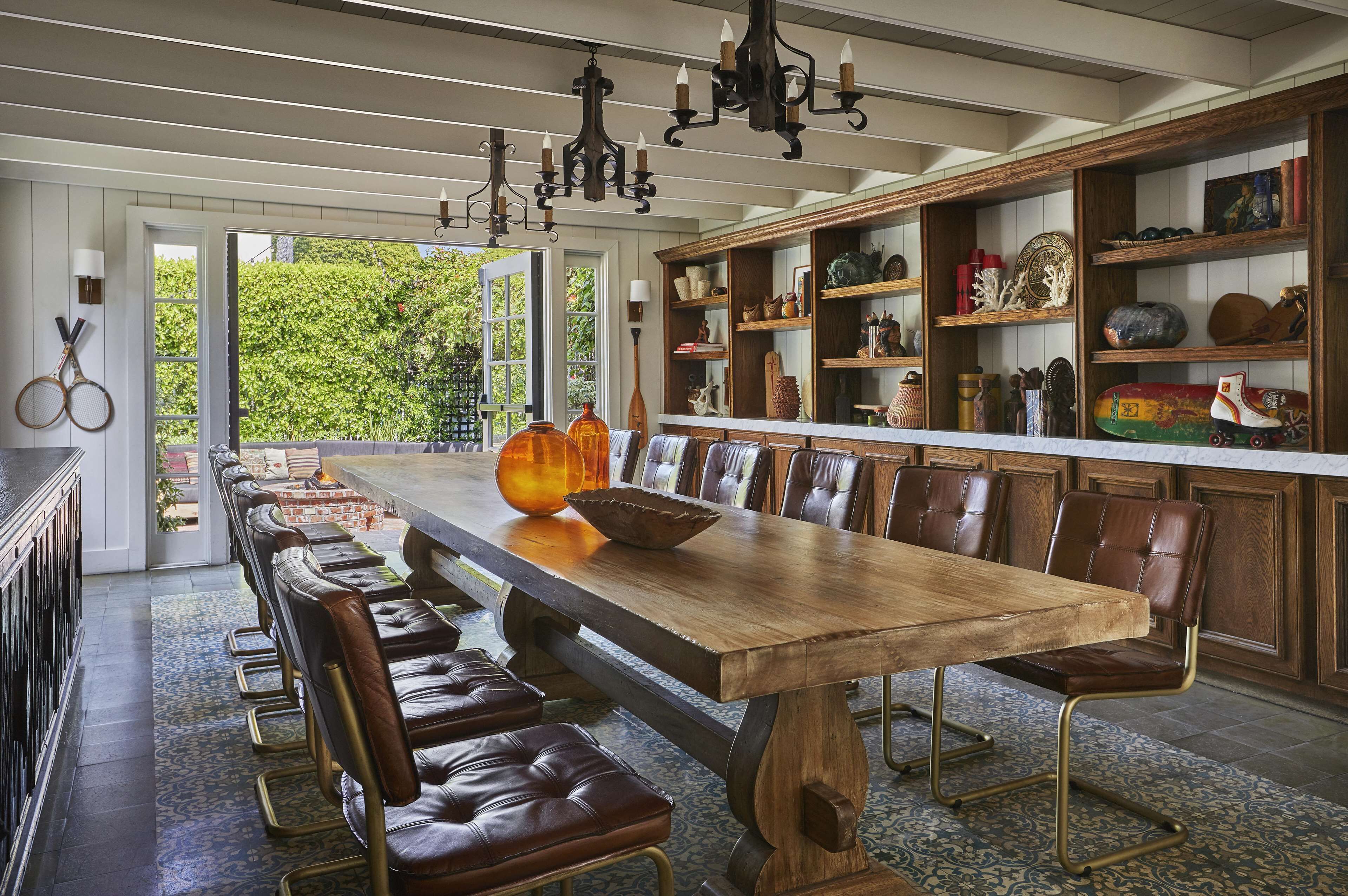 Un lungo tavolo da pranzo in legno con sedie in pelle, un lampadario e scaffali con diversi oggetti decorativi.