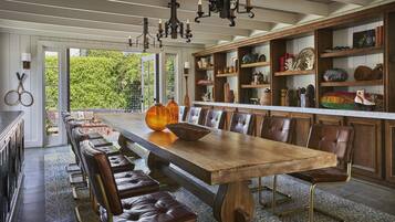 A long wooden dining table with leather chairs, a chandelier, and shelves with various decorative items.