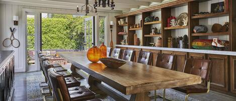 Un lungo tavolo da pranzo in legno con sedie in pelle, un lampadario e scaffali con diversi oggetti decorativi.