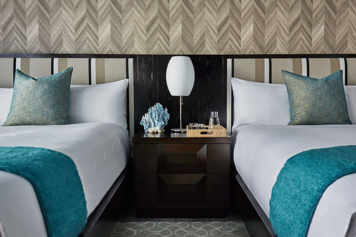 A hotel room with two beds, a nightstand, a lamp, and decorative items.