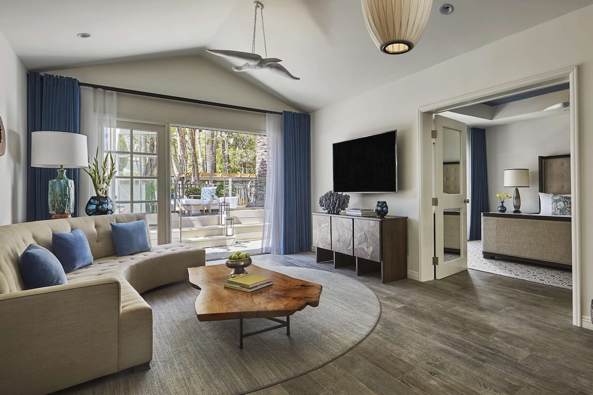 A living room with a sofa, coffee table, and a TV. There is a balcony with a view of palm trees.