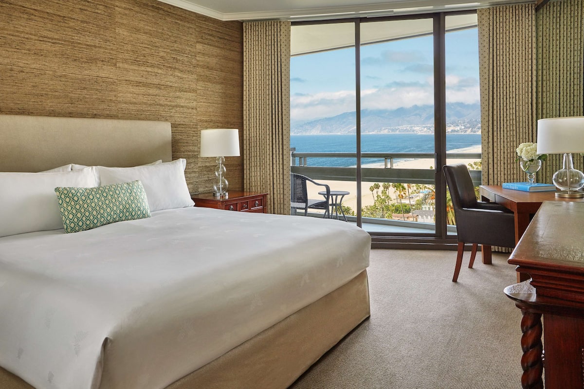 A hotel room with a large bed, a desk, a chair, and a view of the ocean.