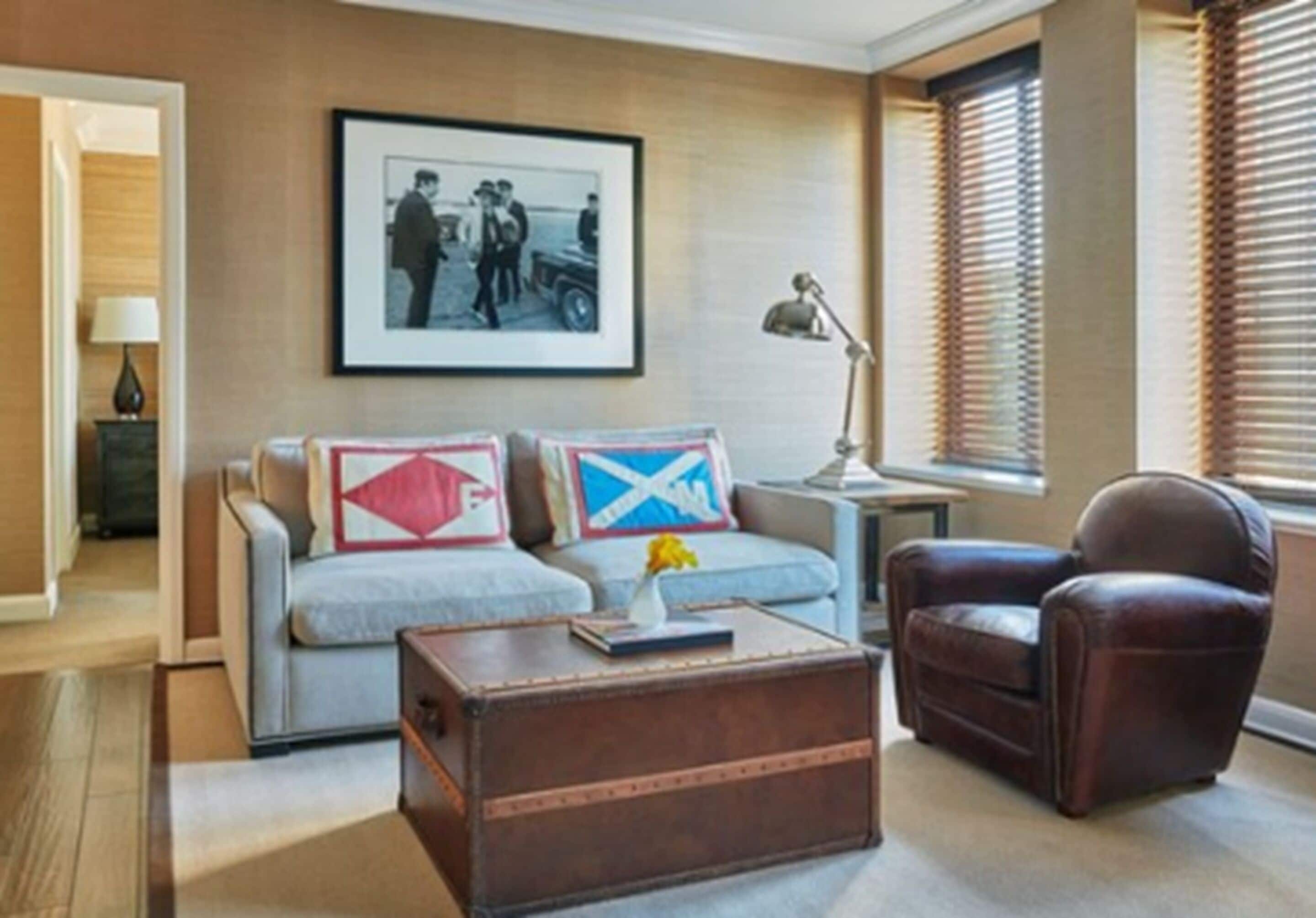 A living room with a sofa, a brown leather armchair, a wooden coffee table, and a framed picture on the wall.