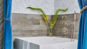 Un baño moderno con una bañera blanca, piso de madera y salpicadero de piedra.
