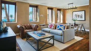 A living room with a leather armchair, a gray sofa with colorful pillows, a coffee table, and a dining area with a metal table and chairs.