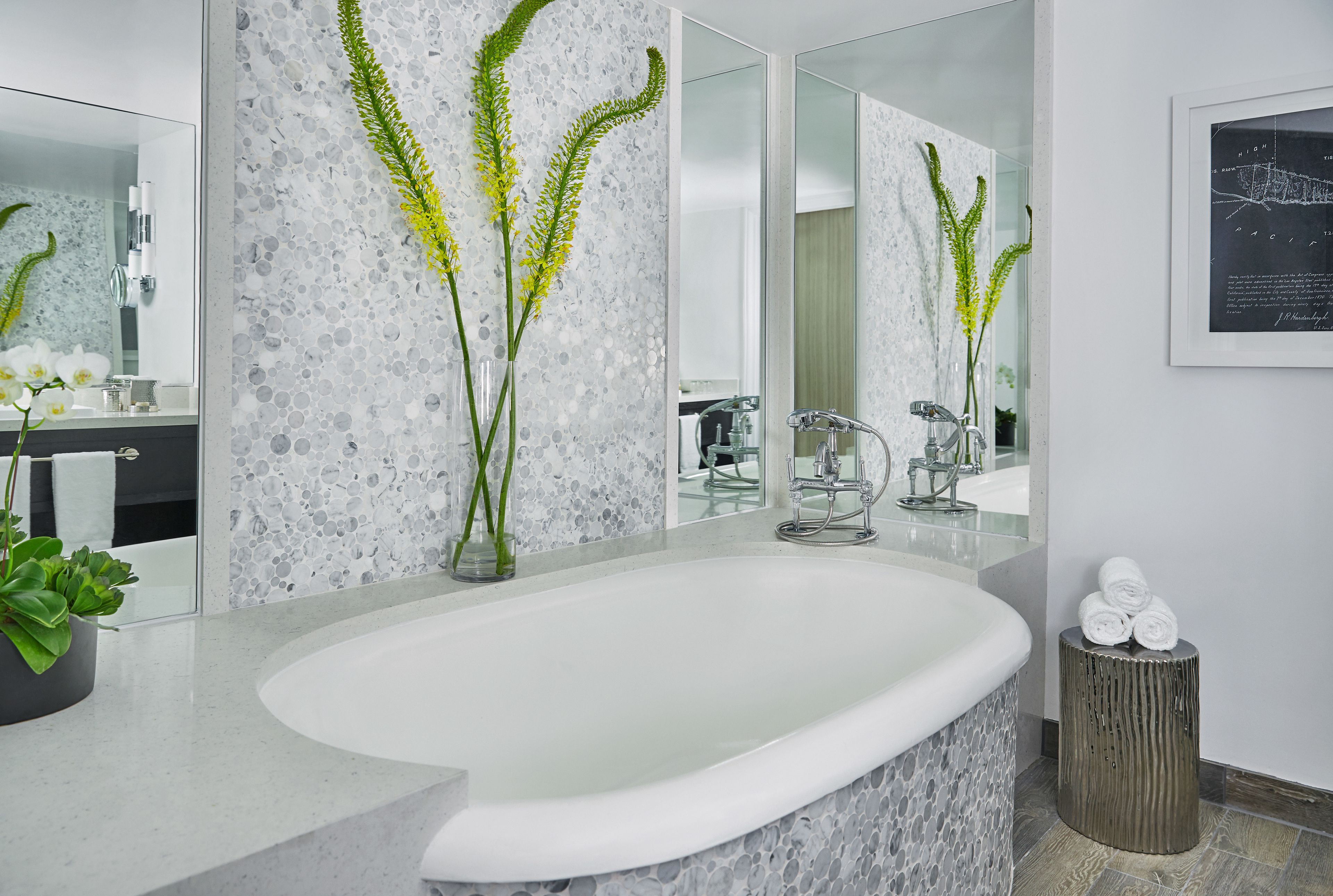 Un baño moderno con una bañera independiente, un espejo grande y plantas decorativas.