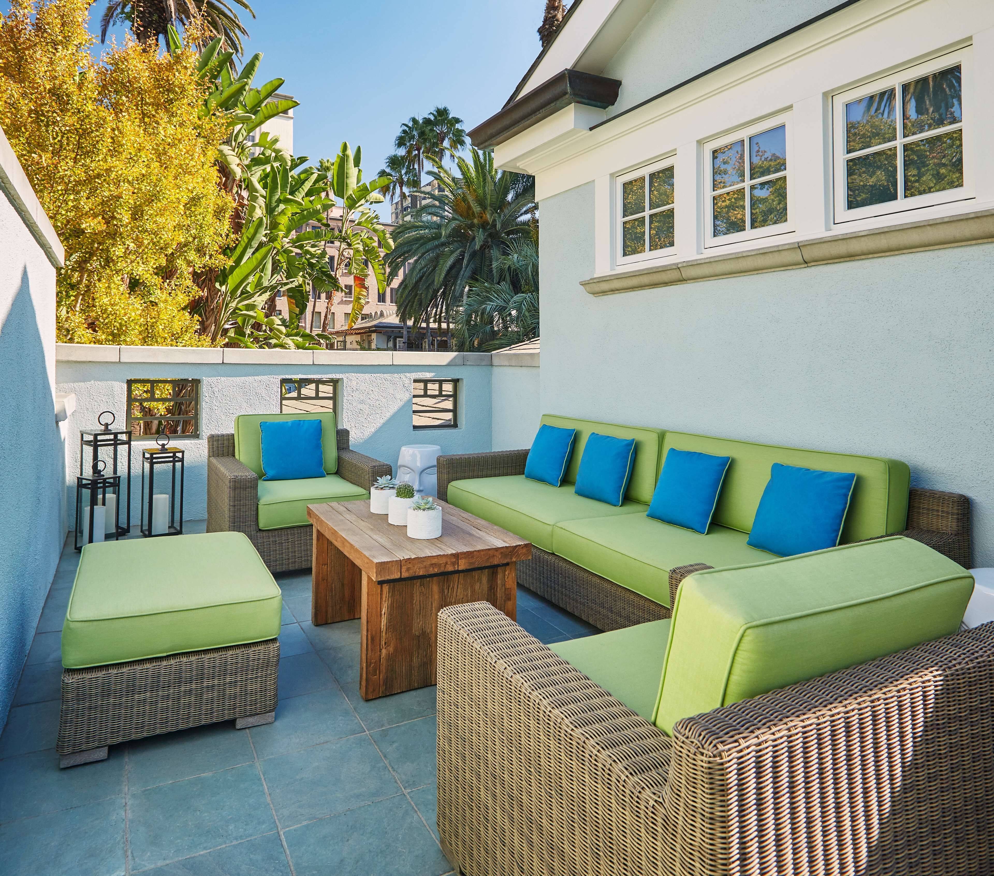 An outdoor patio area with wicker furniture, a wooden table, and a green cushioned sofa with blue cushions.