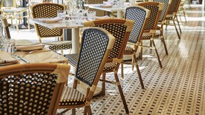 A restaurant with wicker chairs and tables, hanging plants, and a tiled floor.