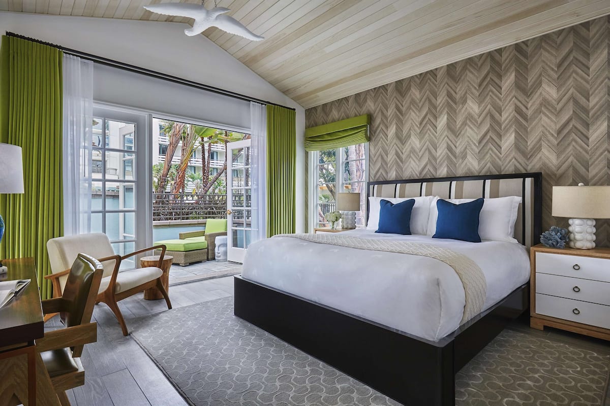 A hotel bedroom with a large bed, a desk, a chair, and a view of the outdoors.