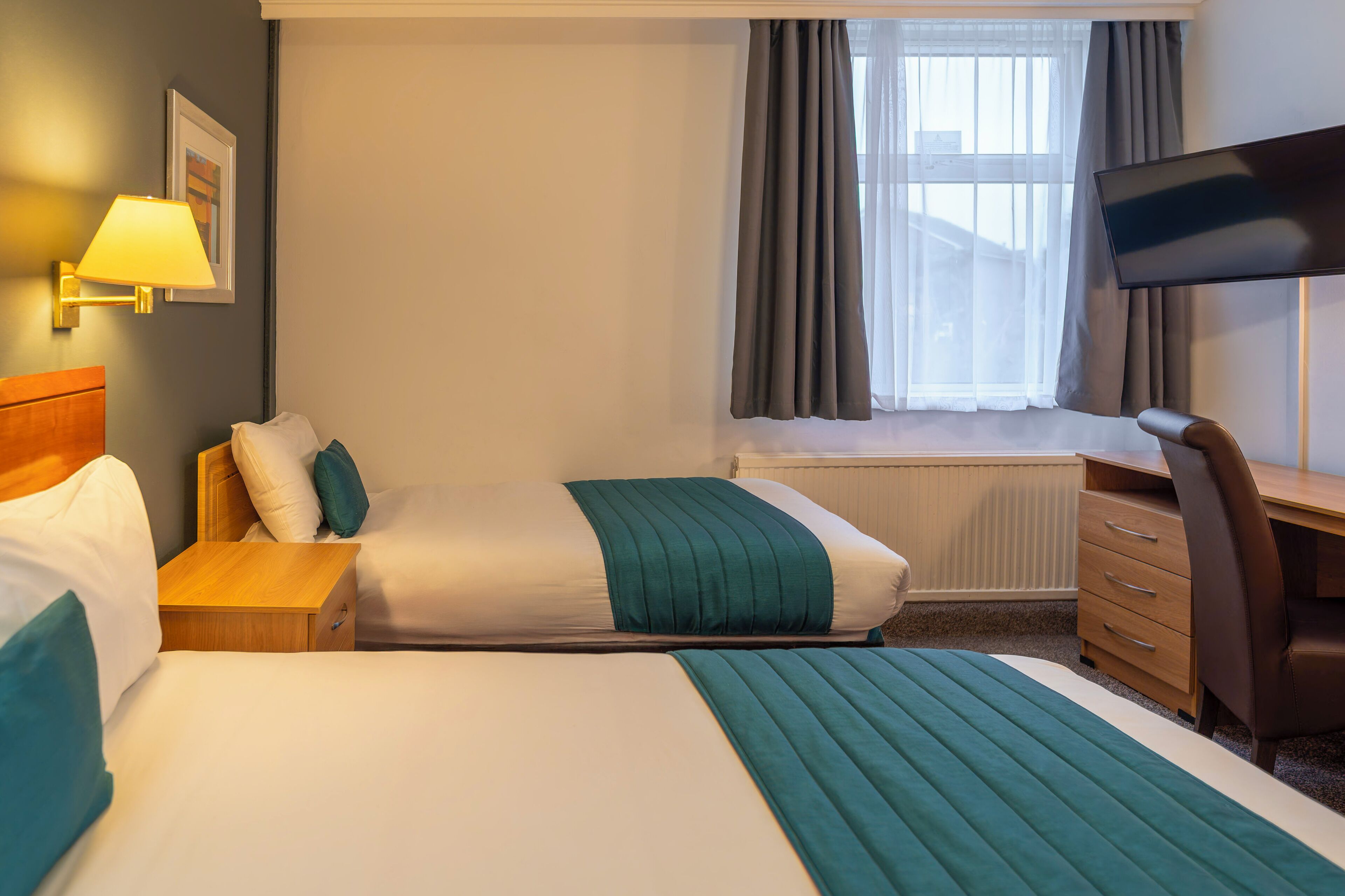 Habitación de hotel con dos camas, un escritorio, una silla, un televisor y una ventana con cortinas.