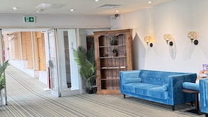 Un vestíbulo de hotel con alfombra estampada, un sofá azul, una estantería de madera y una cámara de seguridad en el techo.