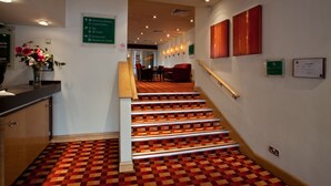 Un vestíbulo de hotel con una escalera, una recepción y señalización.