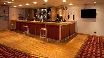 A bar area with stools, a counter, and a television mounted on the wall.