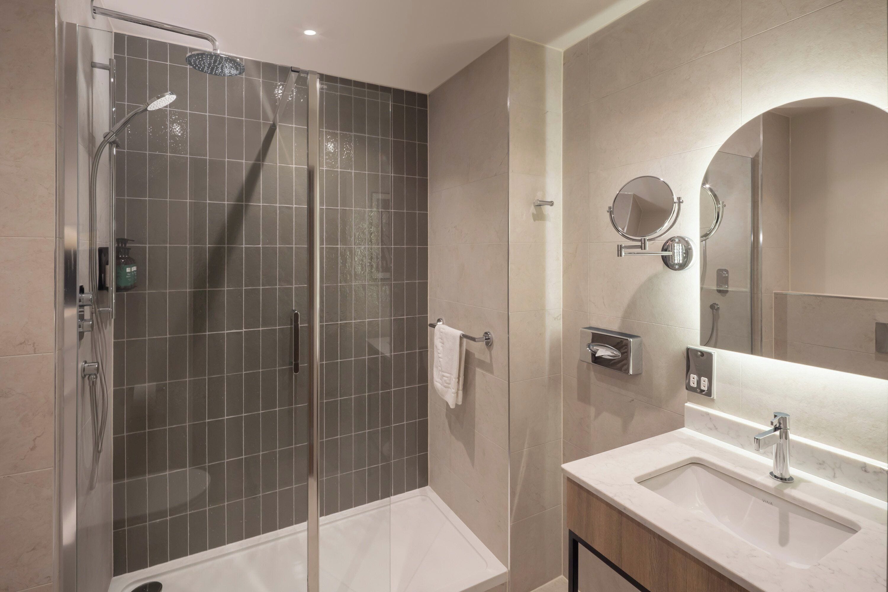 A modern bathroom with a glass-enclosed shower, a vanity with a sink, and a large mirror.