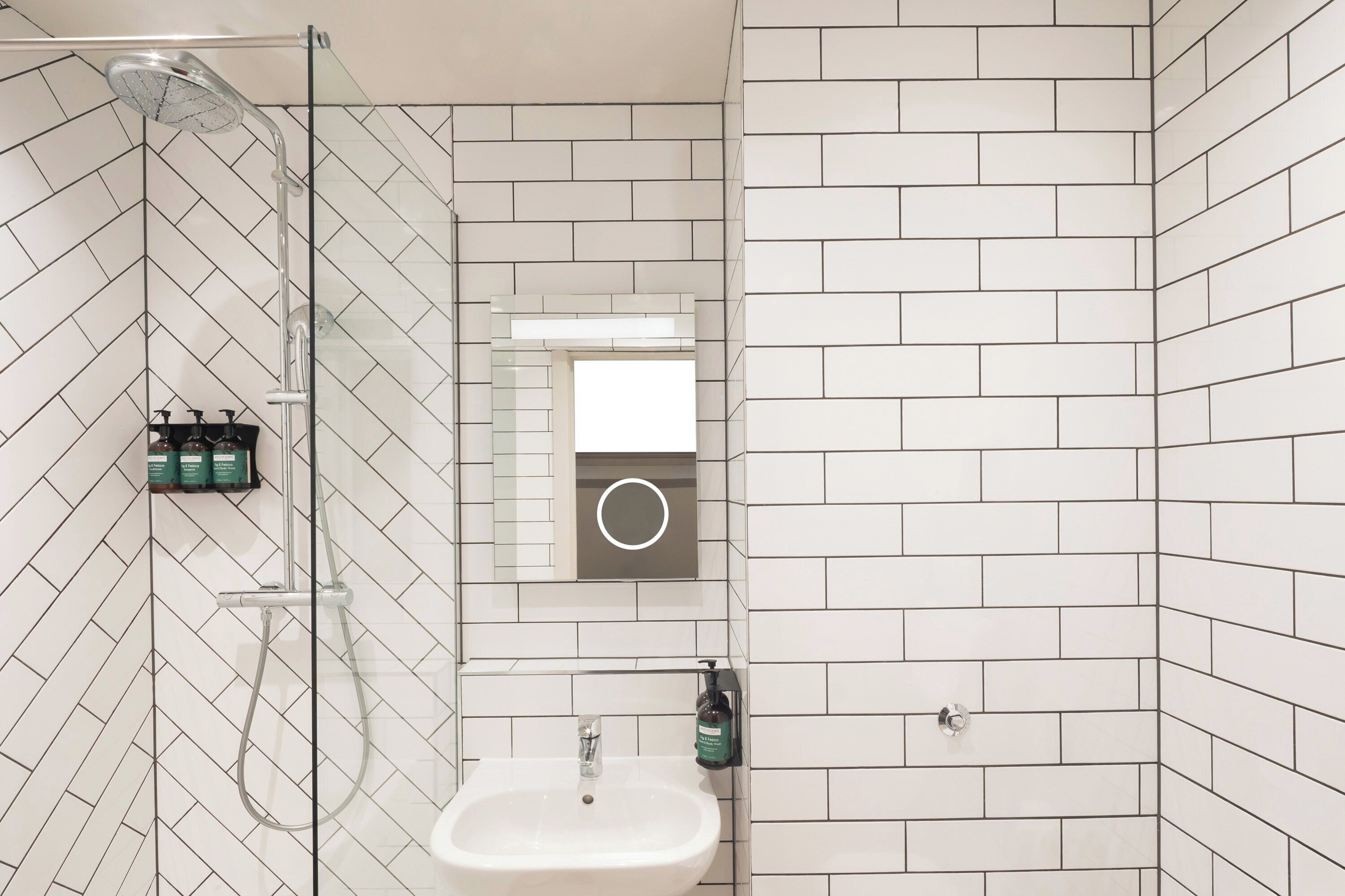 Un baño moderno con cabina de ducha de vidrio, un lavabo blanco y un espejo con luz circular.