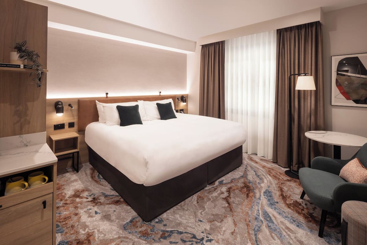 A hotel room with a large bed, bedside tables, a desk, a chair, and a small table.