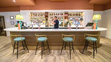 A bar area with a bartender, wooden bar counter, and three bar stools with teal cushions.