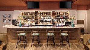 Een bar met een gebogen toonbank, drie krukken en verschillende flessen en glazen.