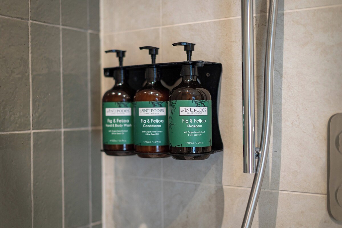 A bathroom with three bottles of Antipodes Fig & Feijoa hand and body wash and conditioner.