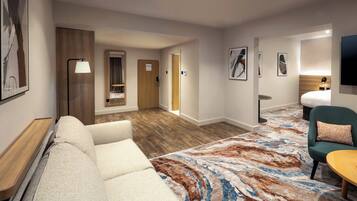 Camera d'albergo con divano, una sedia, un tavolino, televisione e un tappeto decorato.